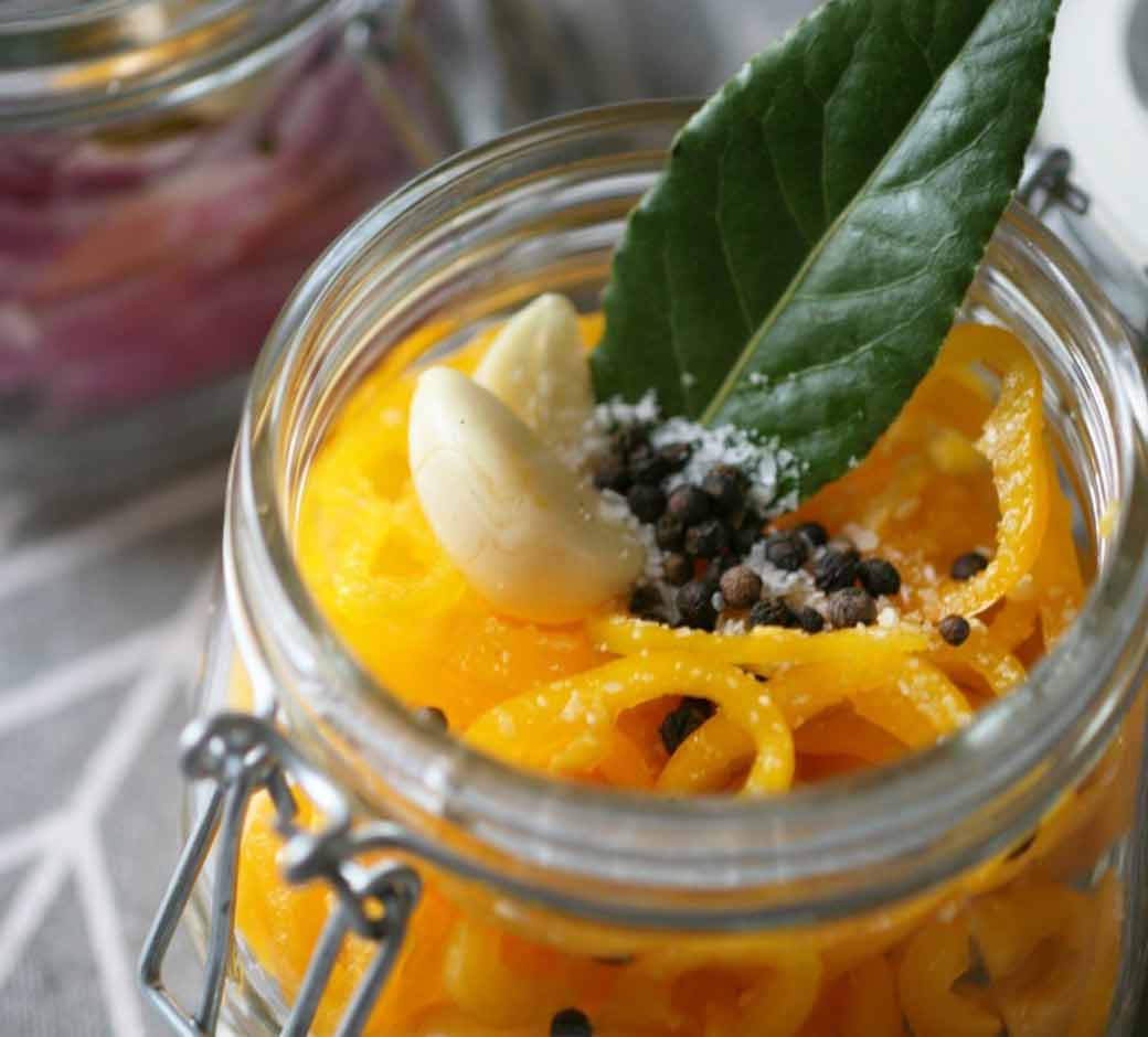 Sliced banana peppers, garlic cloves, peppercorns, bay leaf and salt in a glass jar container