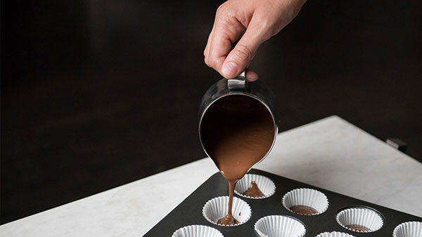 Pouring melted chocolate into paper cups in a muffin tin