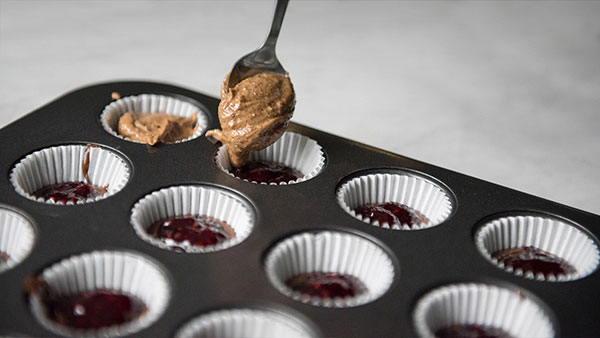 Adding a spoonful of almond butter into a paper cup in a muffin tin