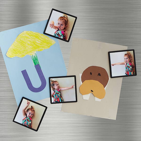 Four framed photo magnets with picture of a girl pointing to the artwork they are holding up on the fridge