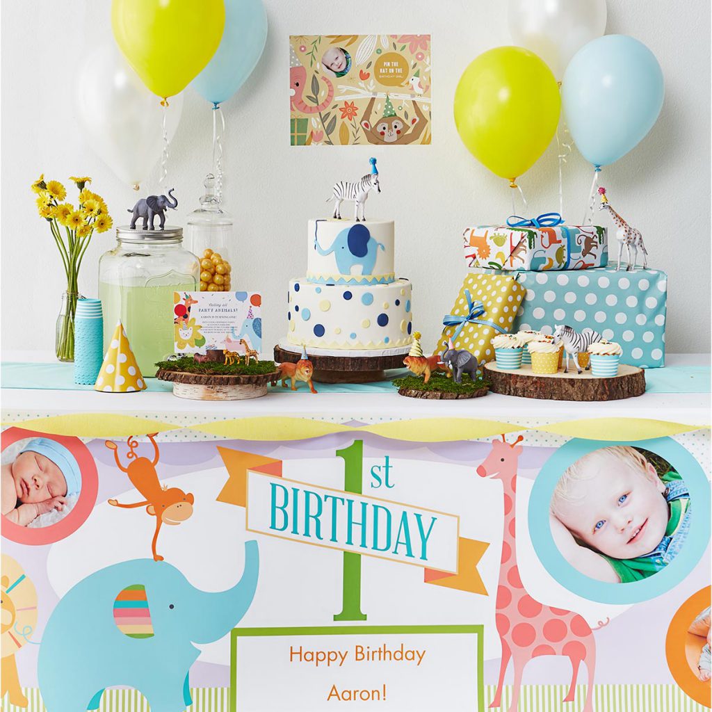 Table decorated with a custom photo banner, and plastic zoo animals, a cake and birthday gifts.