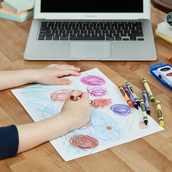 Child creating a drawing next to a laptop