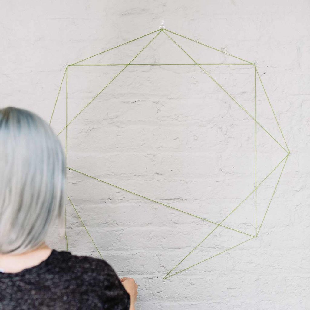 Wrapping green yarn around command hooks to create an octagon
