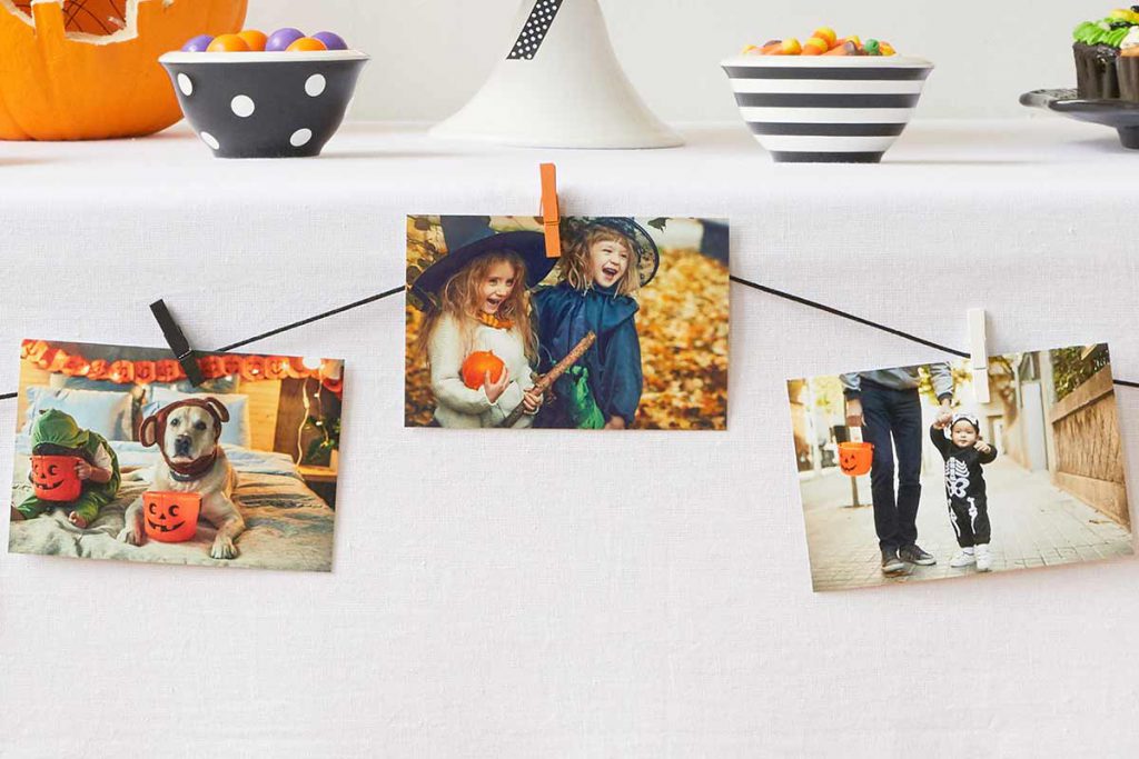Prints of kids and pets trick or treating in Halloween costumes clipped to a string as table decoration.