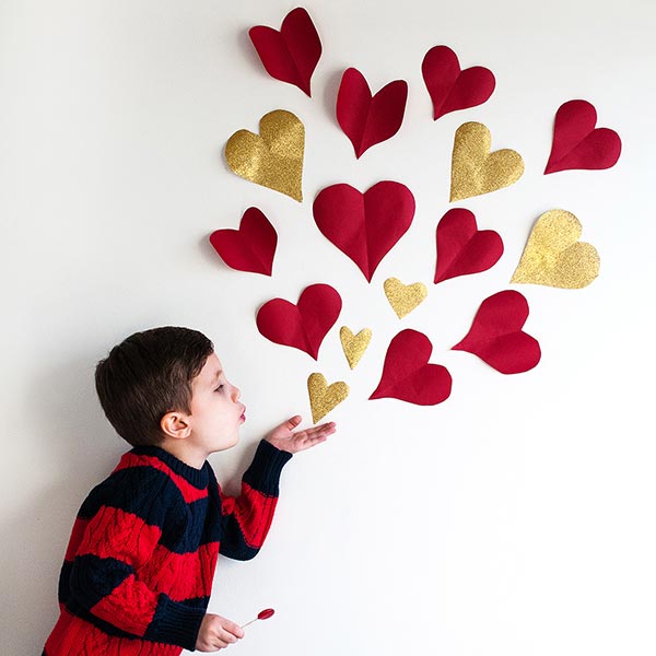 Paper hearts taped to a wall with child pretending to blow them out of his palm