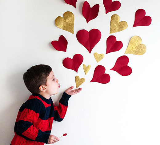 Photo Valentine's Day DIY project, child pretending to blow paper hearts out of his hand