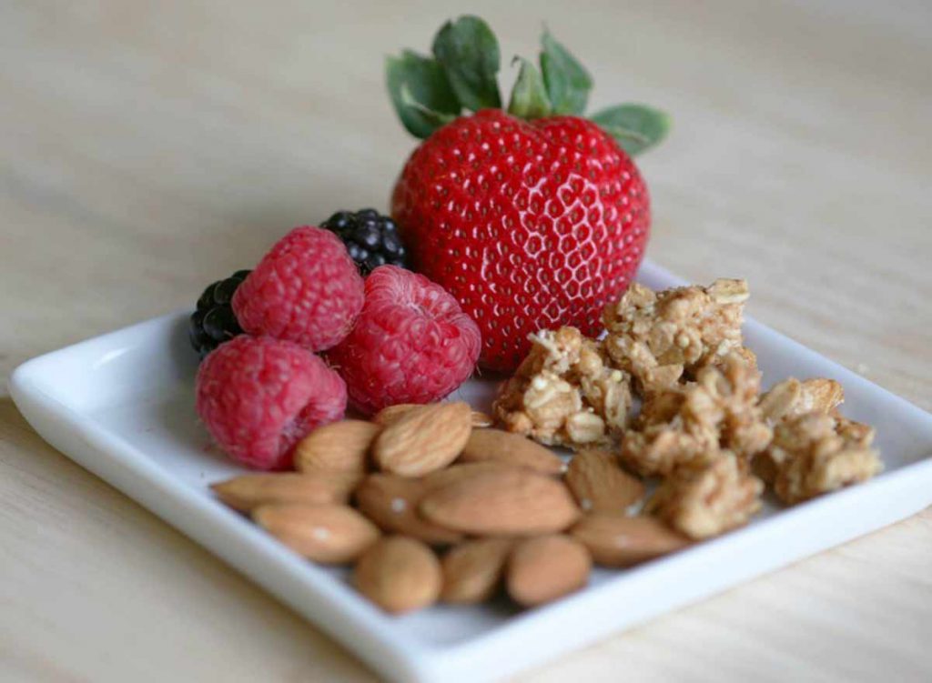 A plate of almonds, granola, raspberries, blackberries and strawberries, sitting on a table